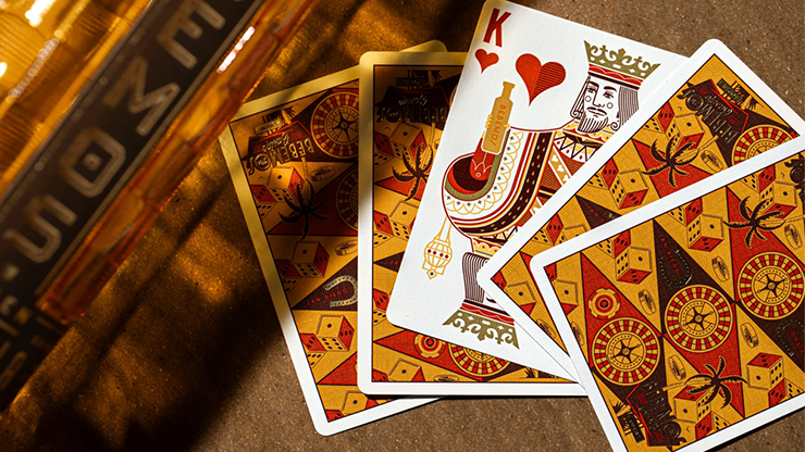 Bebemos Casino playing cards by theory11 featuring King of Hearts and retro geometric card backs displayed on a wooden table beside a Bebemos tequila bottle in warm golden lighting