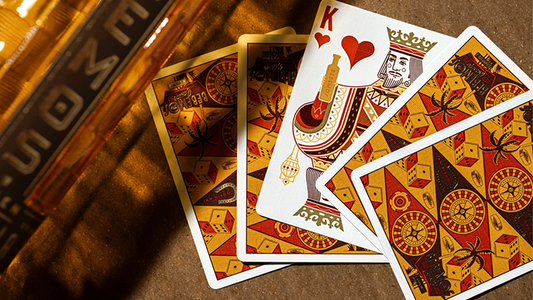 Bebemos Casino playing cards by theory11 featuring King of Hearts and retro geometric card backs displayed on a wooden table beside a Bebemos tequila bottle in warm golden lighting