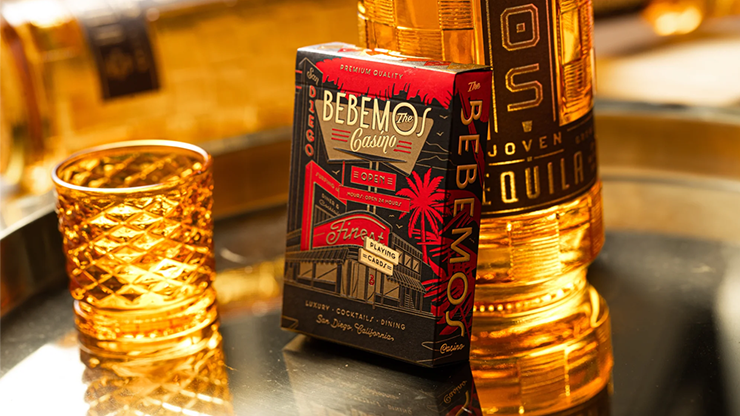 Bebemos Casino playing cards by theory11 retro deck displayed on a reflective bar tray beside a tequila bottle and textured cocktail glass with warm golden lighting