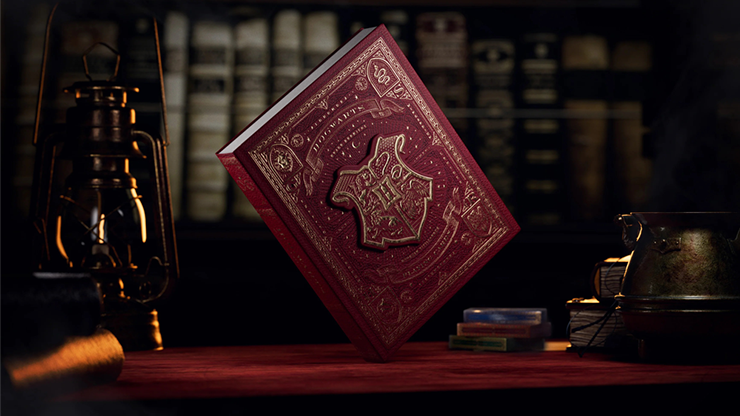 Harry Potter playing cards box set by theory11 featuring a red Hogwarts-themed collector book box displayed on a wooden table with lantern and books.