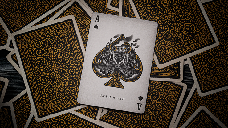 Ace of Spades card from Peaky Blinders playing cards by theory11 featuring Small Heath emblem design displayed among ornate gold card backs on a dark wooden surface