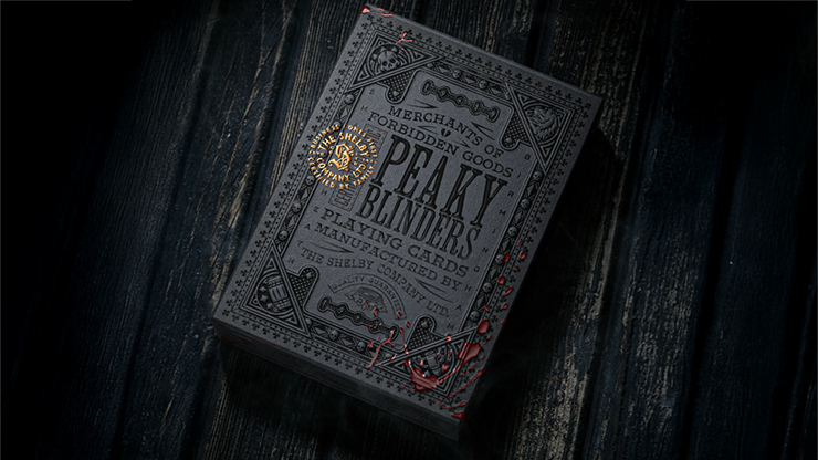 Peaky Blinders playing cards by theory11 premium collector deck box with antique gold foil details displayed on a dark wooden surface