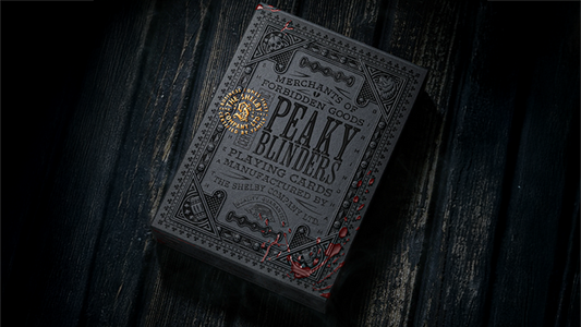 Peaky Blinders playing cards by theory11 premium collector deck box with antique gold foil details displayed on a dark wooden surface